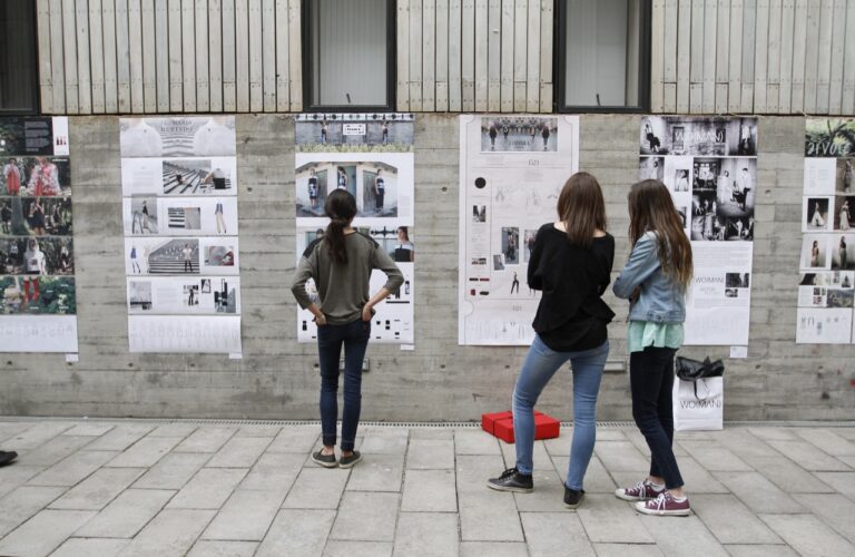 Tres mujeres observando diseños pegados en una pared de cemento.